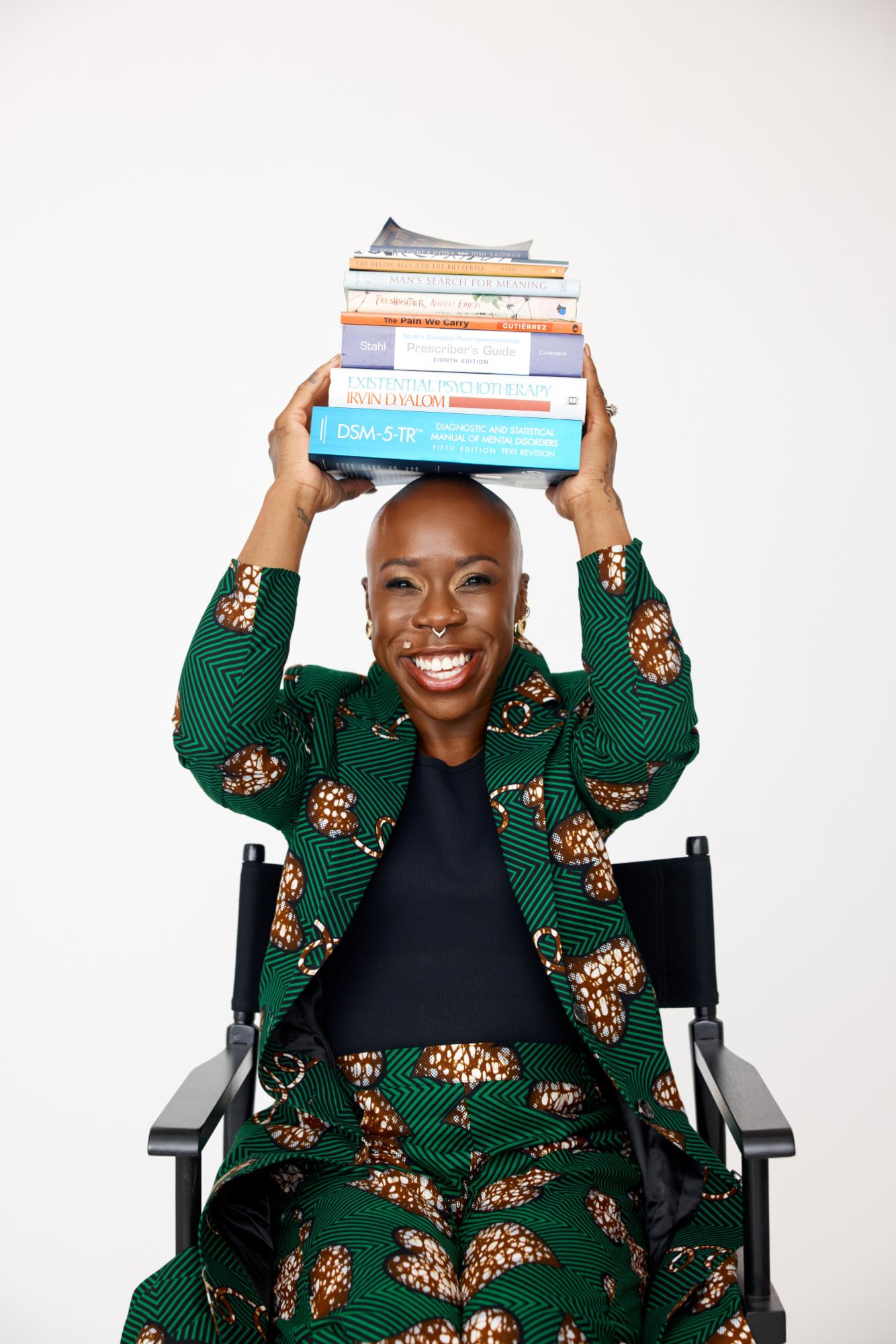 Person in a green patterned outfit holding books above their head against a white background